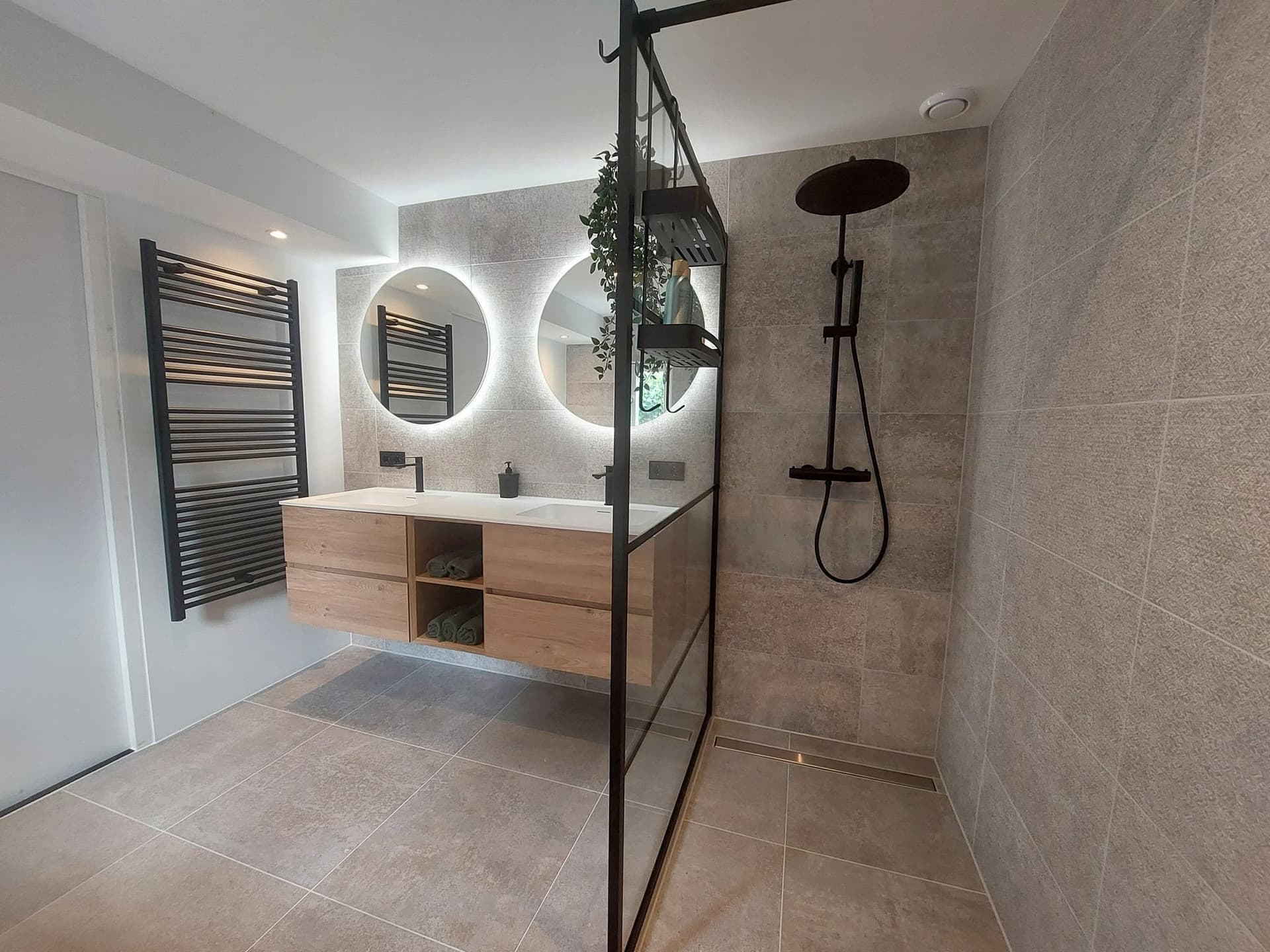 Badkamer met eiken wastafelmeubel, twee ronde spiegels en een zwart stalen douchescherm