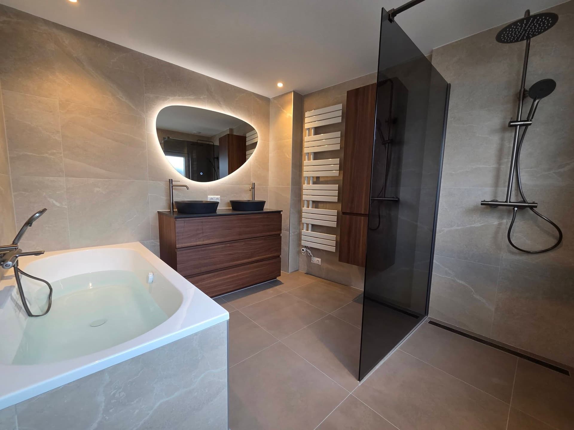 Badkamer met notenhouten meubel, ligbad en rookglas douchescherm